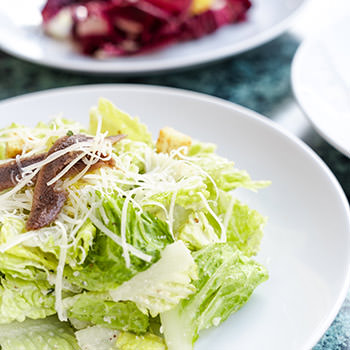 A plate of Caesar Salad on a green marble table top. 
